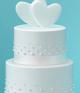 White wedding cake with hearts on top, in front of baby blue background