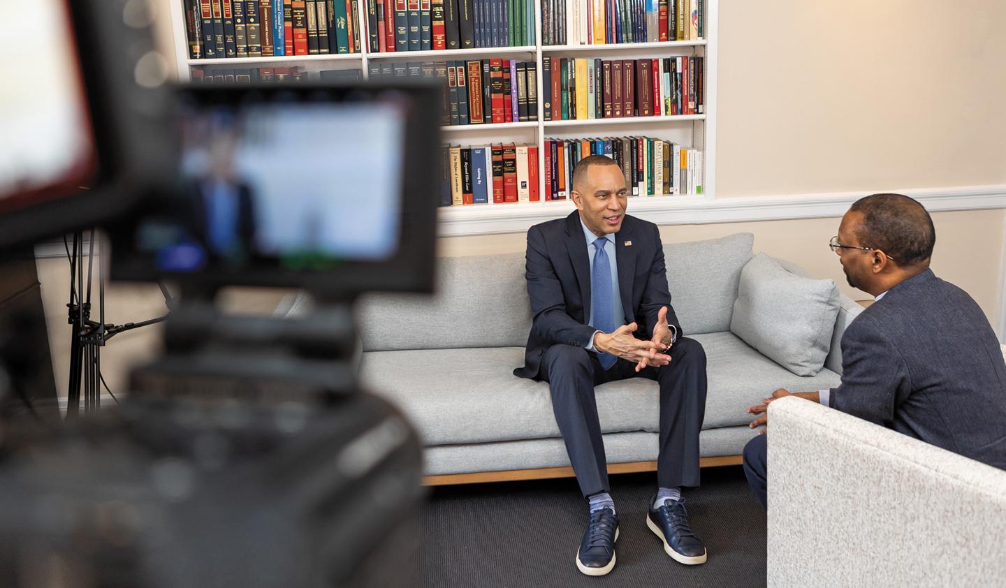 Hakeem Jeffries sits on a couch, talking with Troy McKenzie while a video camera films